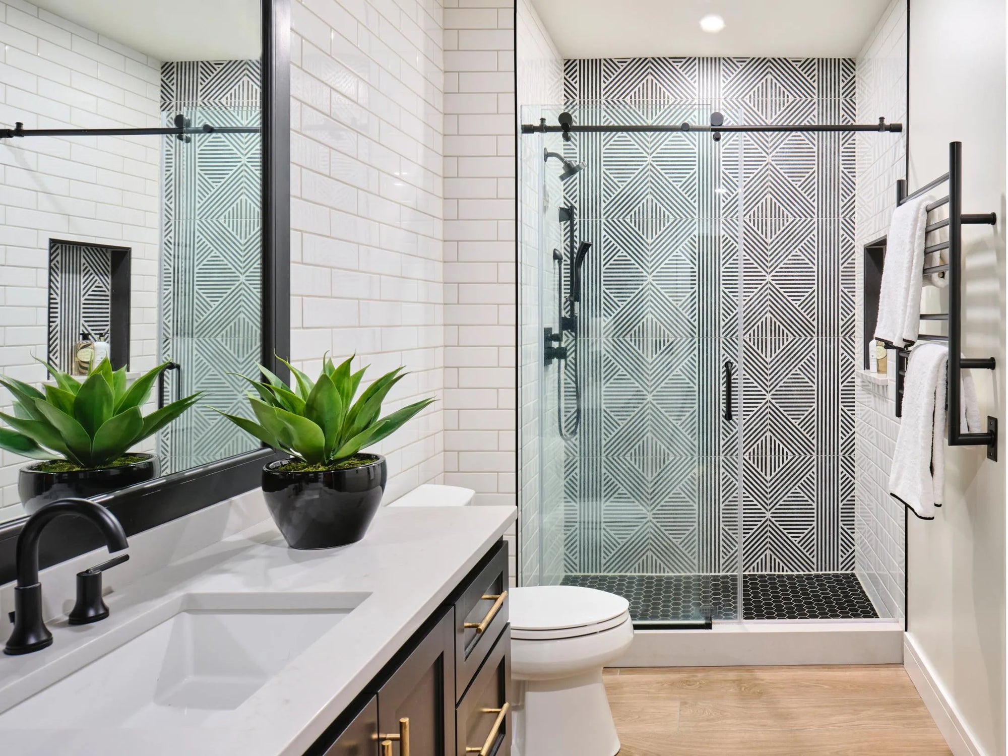 Modern bathroom with a sliding glass shower door, black fixtures, white floating vanity, and green plants for a sleek look.