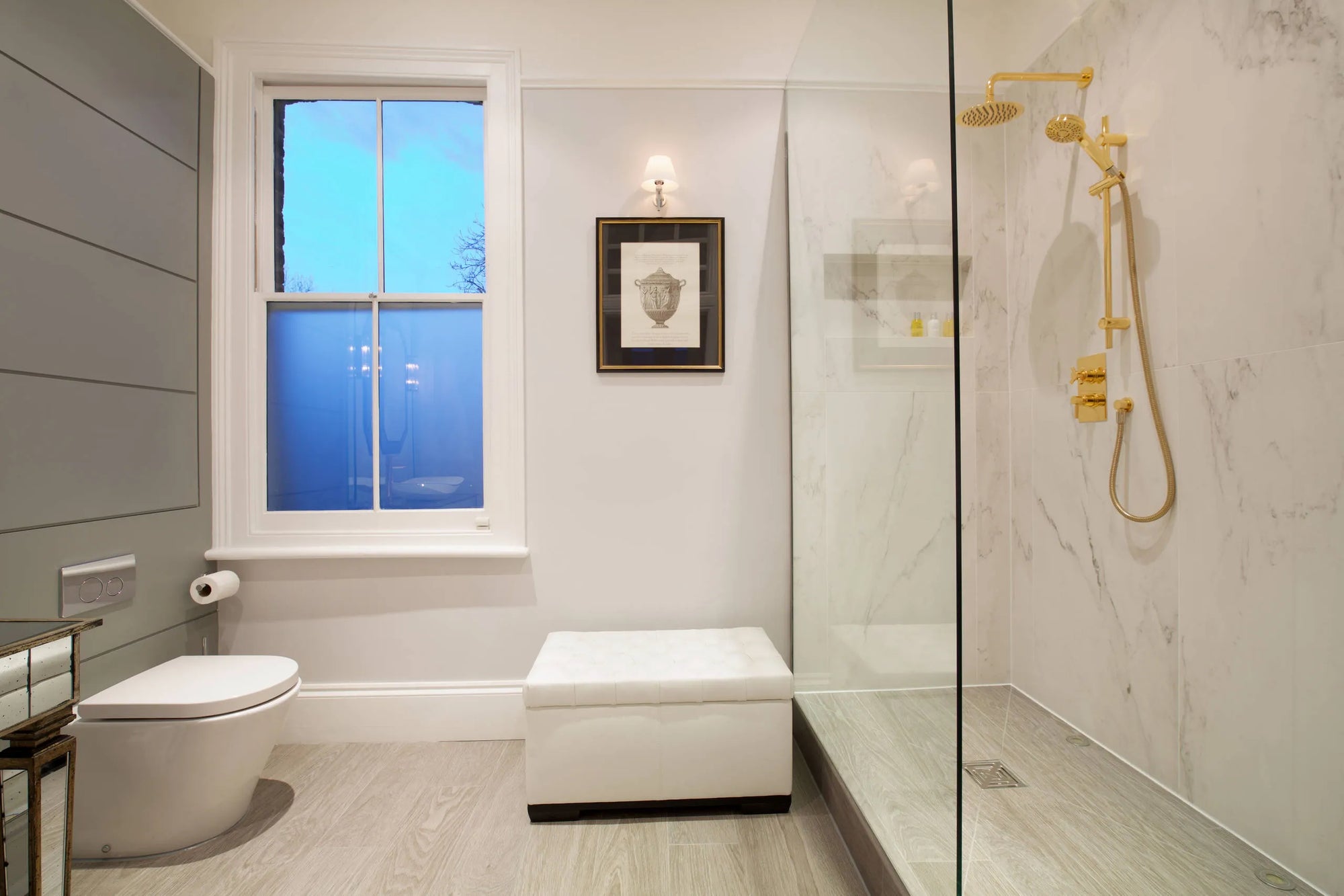 Modern bathroom with a glass-enclosed shower featuring gold fixtures, marble walls, and natural light.