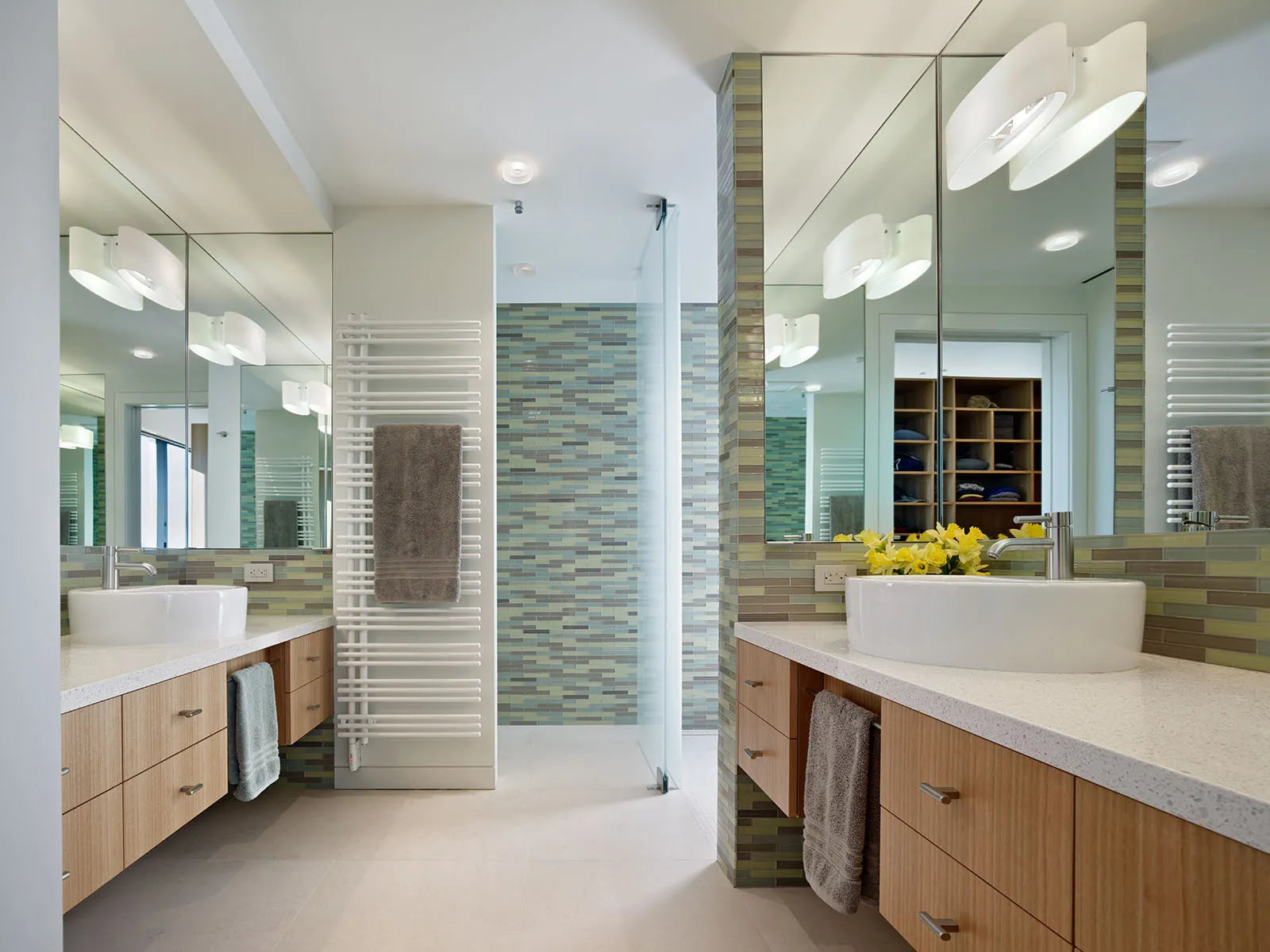 Sleek towel warmer in a modern bathroom with dual vanities, light wood cabinetry, and large mirrors.