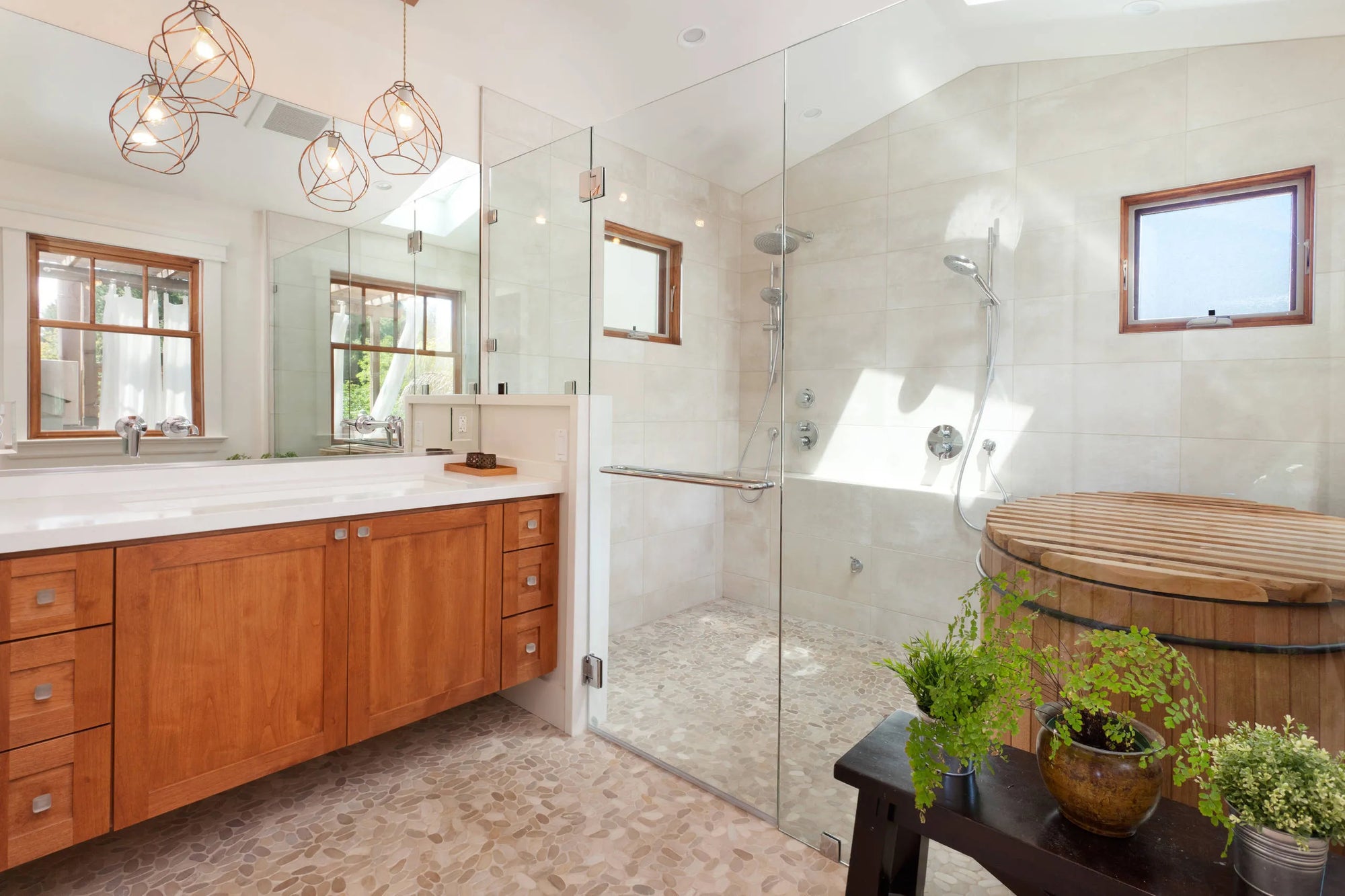 Spacious glass-enclosed shower system in a luxurious bathroom with a double vanity, freestanding tub, and natural light from large windows.