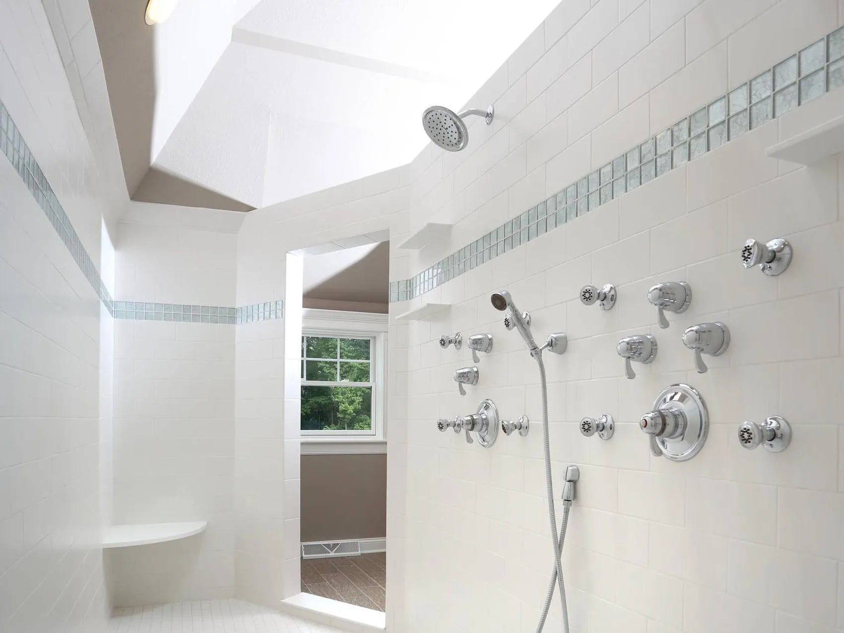 Luxurious modern bathroom with overhead rain shower and elaborate shower valve system with body sprays, white tiling, and skylight.