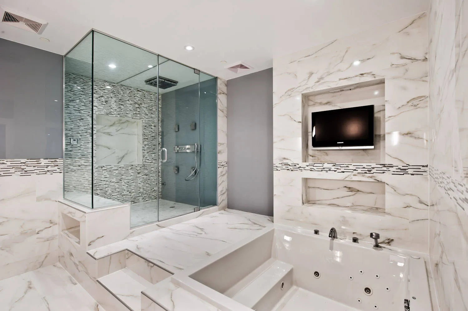 Luxurious bathroom with a multi-jet Jacuzzi tub, marble tiles, glass shower, and wall-mounted TV for a spa-like retreat.