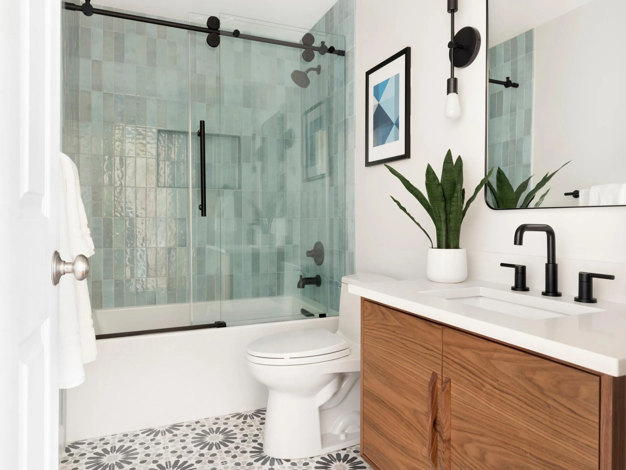 Modern bathroom with a white alcove tub, black-framed glass shower door, teal subway tiles, and hexagonal floor tiles.