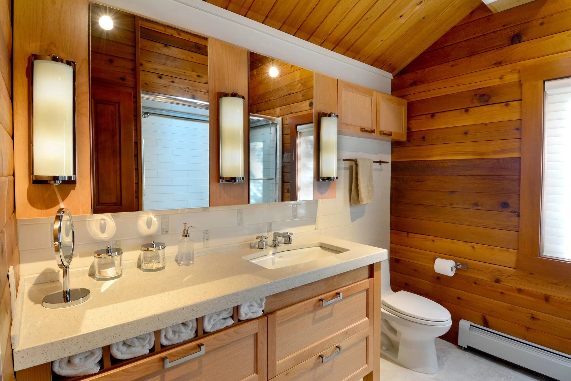 A well-lit bathroom with wooden walls, a double-sink vanity, and a white toilet, creating a cozy and functional space.
