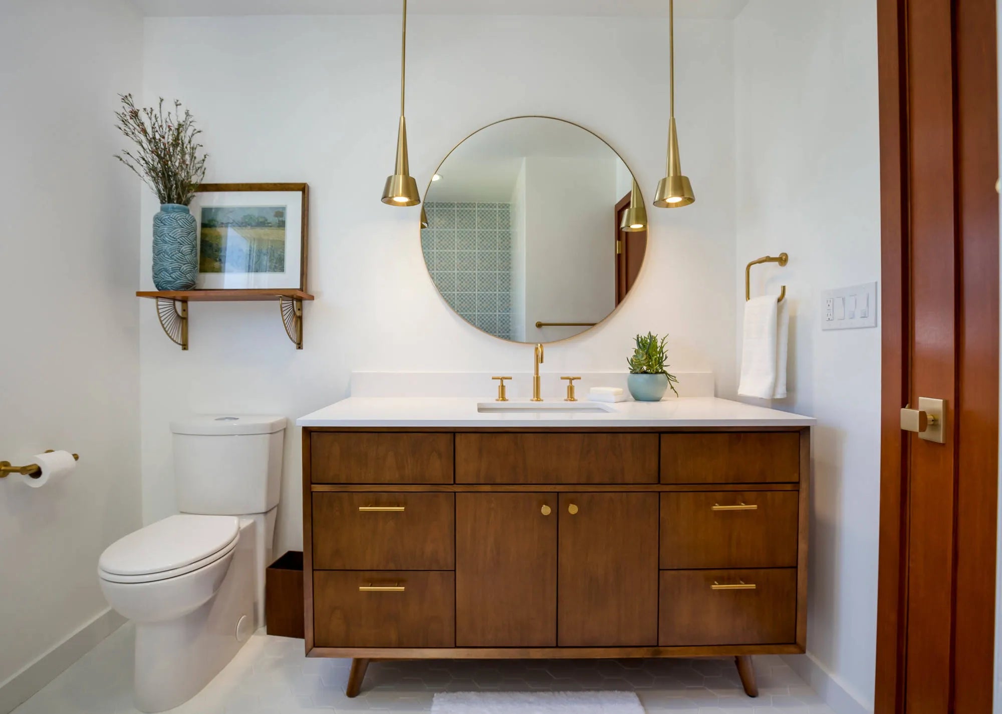 Bathroom round mirror above a wooden vanity with gold pendant lights in a minimalist, modern bathroom.
