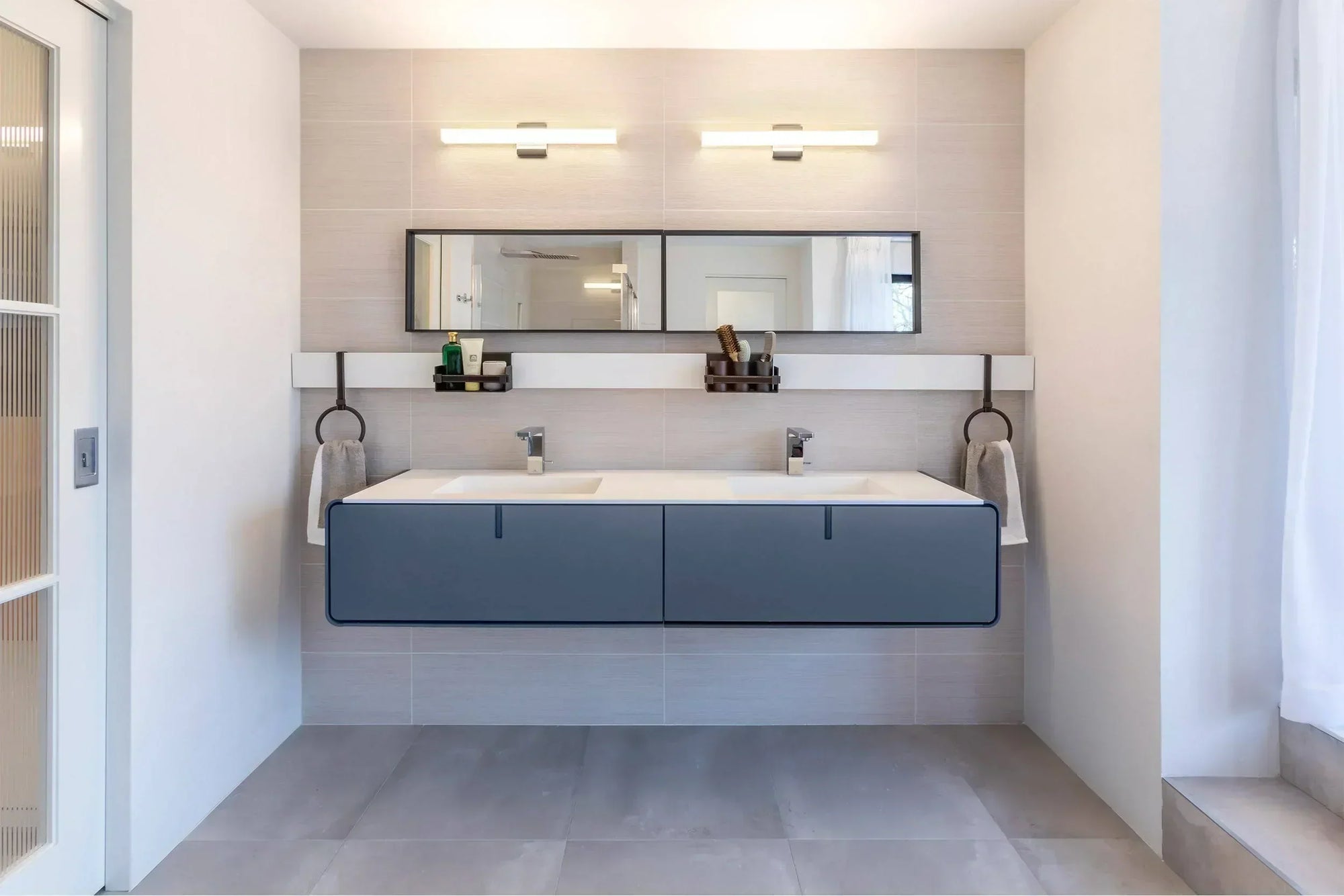Modern bathroom with floating double vanity, blue cabinets, and LED lights over a large mirror.