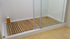 A wooden shower base mat inside a shower enclosure, showcasing a unique natural aesthetic, demonstrating how different shower base colors and materials can enhance bathroom design.