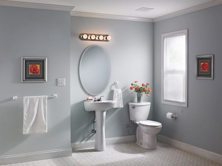 Beveled mirrors for bathroom in an oval shape above a pedestal sink, with minimalistic decor and soft natural light from a nearby window.