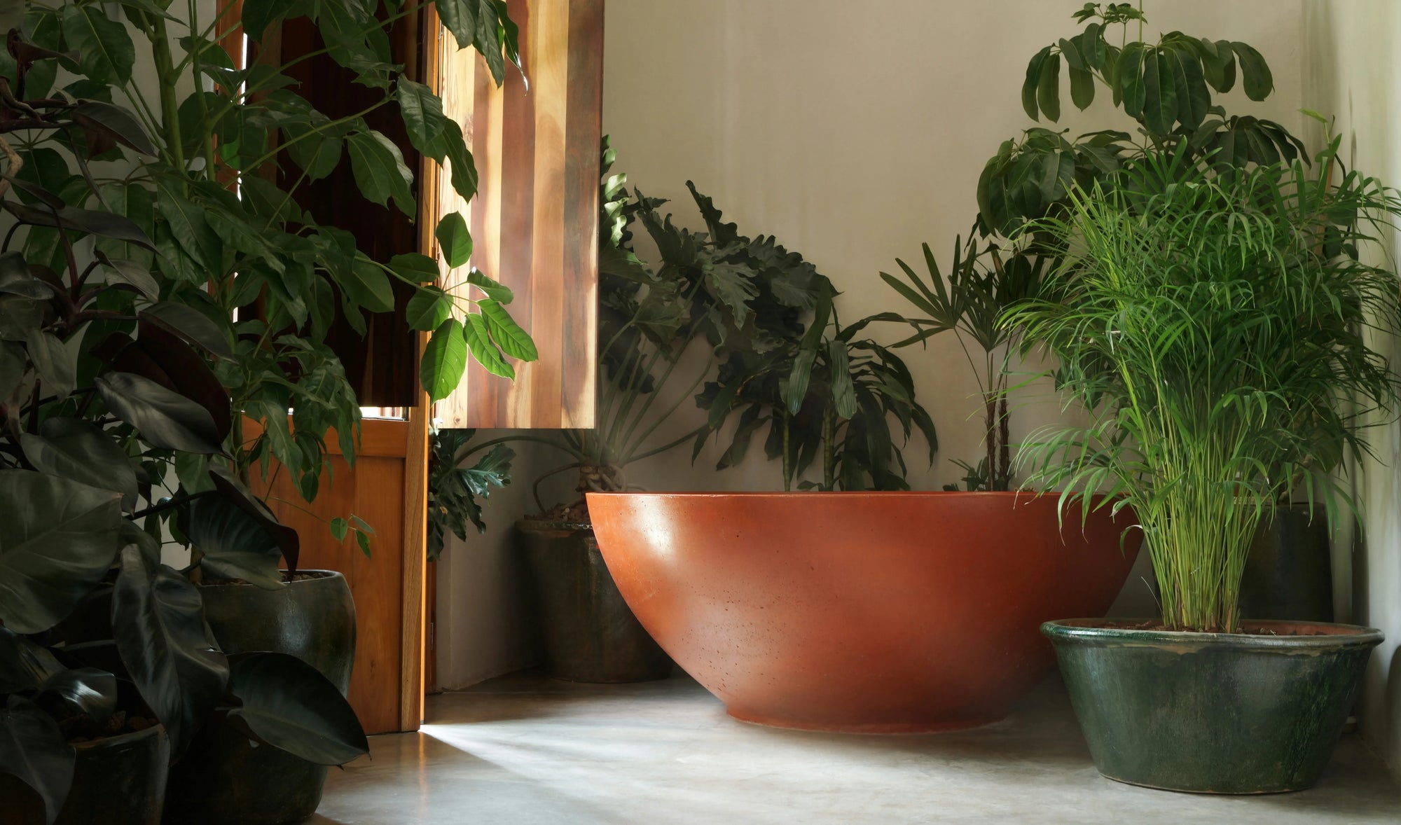 A serene bathroom with a freestanding copper bathtub surrounded by lush shower plants, natural light, and wooden accents.