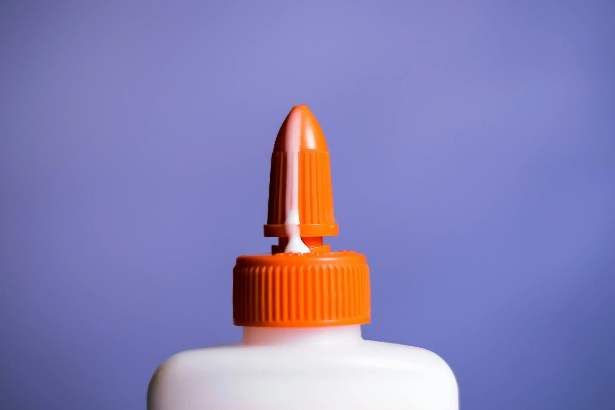 Glue for glass with precision tip dispensing adhesive from orange-capped bottle on purple background.