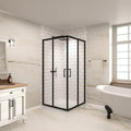Corner black framed double sliding glass shower enclosure in a modern bathroom setting with white tile walls and freestanding bathtub.