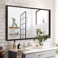 Noir Series black rectangular beveled-edge mirror installed in a modern minimalist bathroom, reflecting white tiles, wood accents, and greenery.