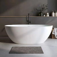 Matte white Abyss Series curved solid surface resin soaking tub, freestanding, in a minimalist bathroom setting.