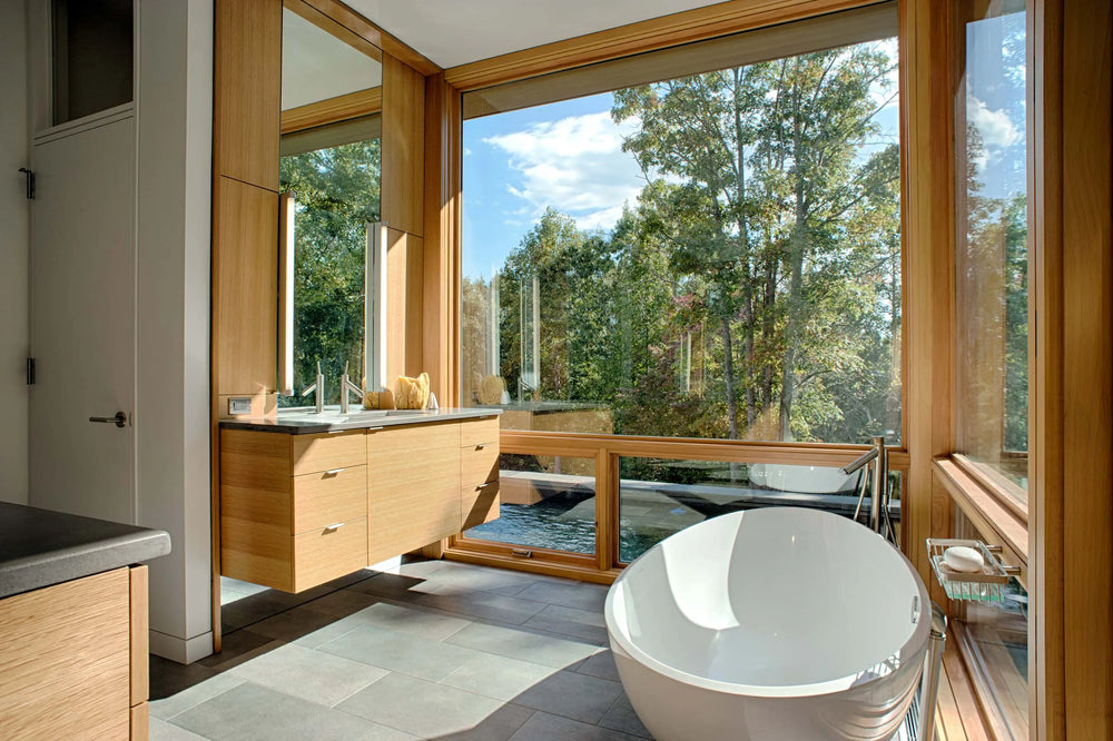 Bright modern bathroom with freestanding bathtub, floating wood vanity, and large windows.