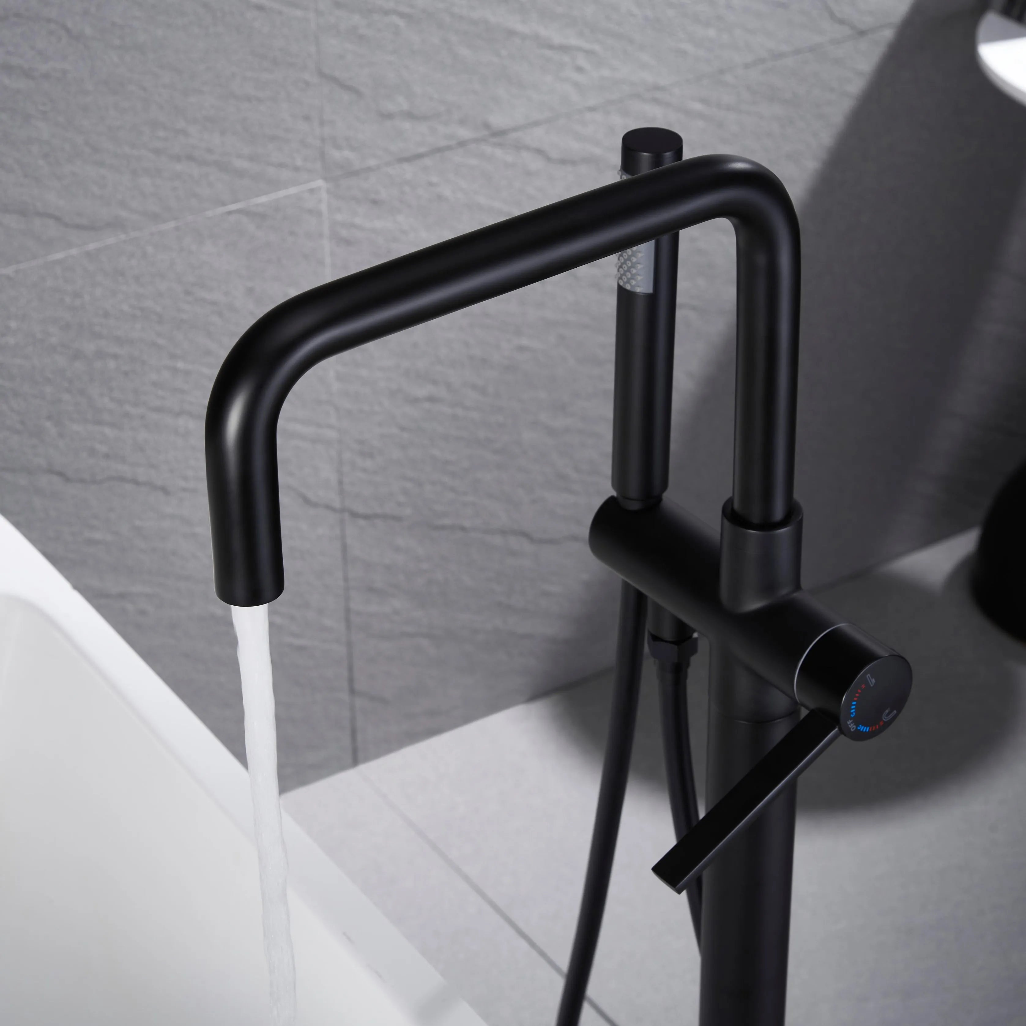 Matte black freestanding tub faucet with a curved rotating spout filling a white bathtub, handheld shower, and single lever control.