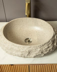 A beige stone-textured vessel sink with a rough exterior and smooth interior, set on a white countertop beneath a brass faucet. |ACE DECOR
